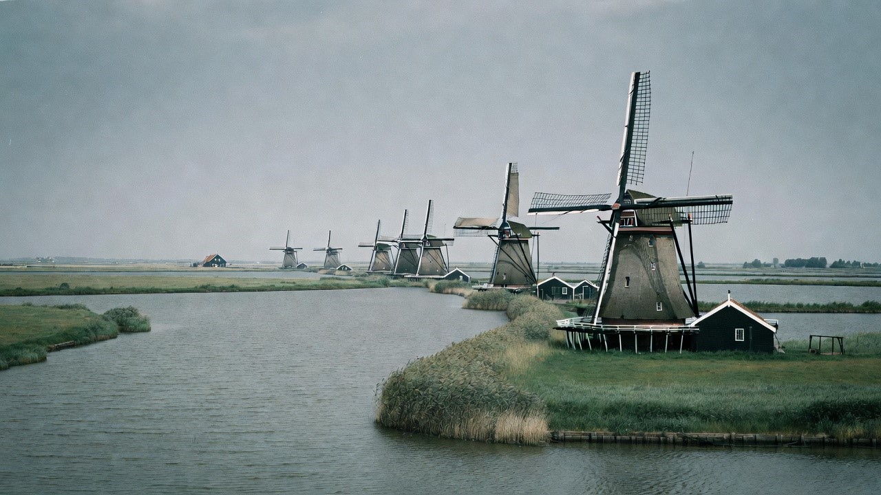 A row of Dutch windmills draining flat polder land along a canal